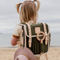 Child with a green backpack and pink hat on a beach