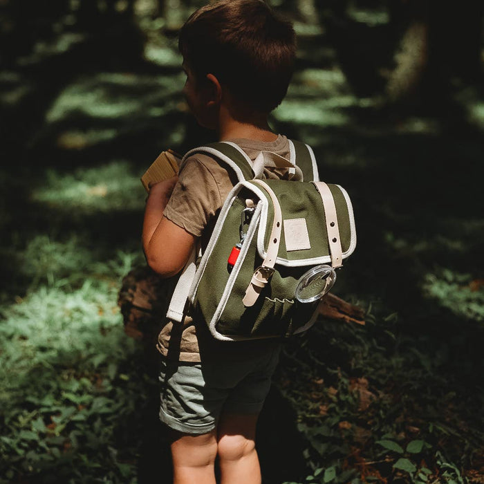 Child with a green backpack walking through a forest