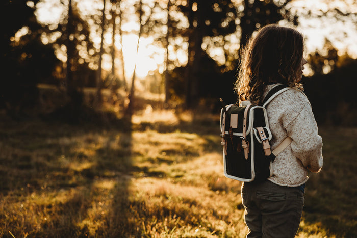 Child with a backpack walking through a forest at sunset