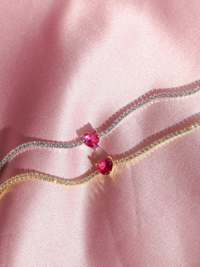 A close-up image of a sterling silver bracelet with pink heart zirconia stones, displayed on a pink fabric surface.