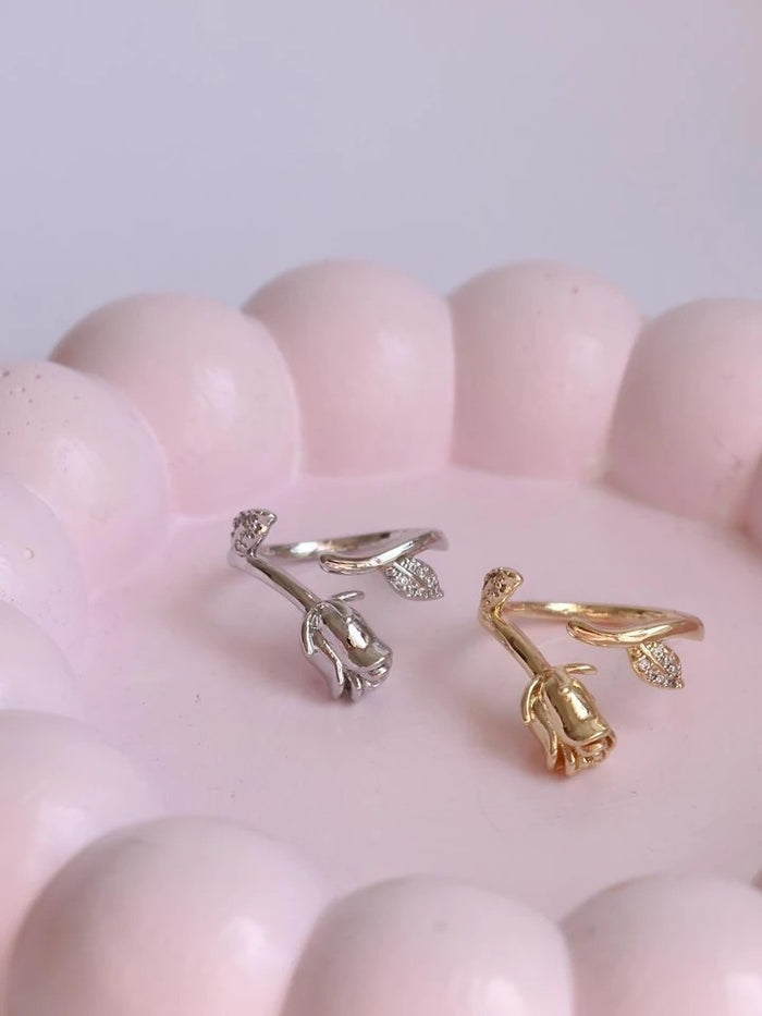 Belle Rose Shine Ring, Gold and silver rose-shaped earrings on a pink surface