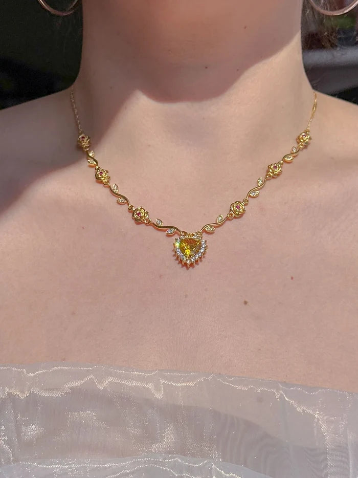 A person wearing a gold-colored Belle's Rose Heart Necklace with a rose-shaped pendant, displayed against a neutral background.
