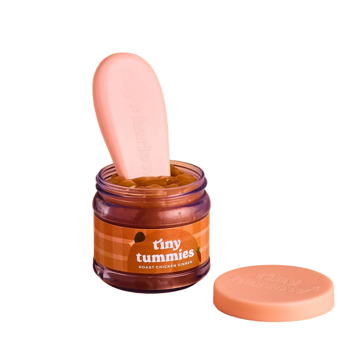 Jar of 'tiny tummies' baby doll pretend play food with a pink spoon on a beige background