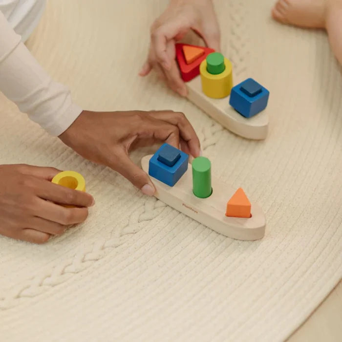 Children playing with colorful wooden shape sorting toys on a textured surface.