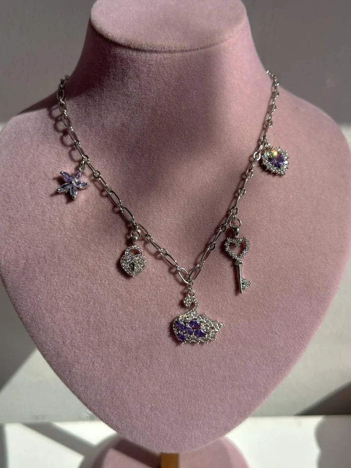 Purple Swan Charm Necklace silver-colored charm necklace with multiple charms including a heart and a key, displayed on a pink mannequin.