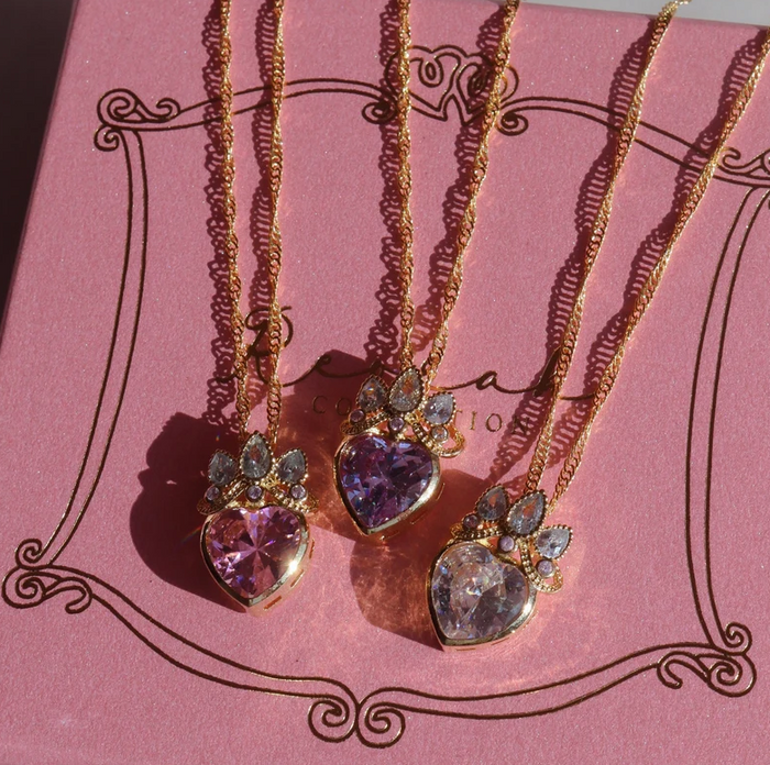 Rapunzel Crown Heart Necklace,  with a heart-shaped pendant, displayed on a pink background with floral patterns.