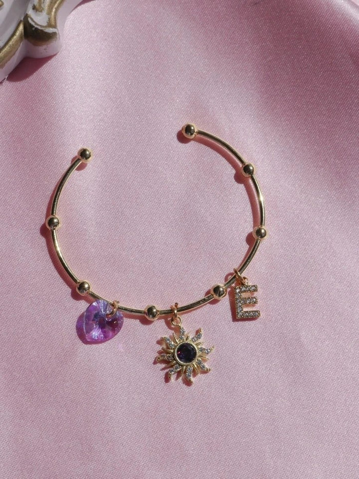 Rapunzel Sun Letter Charm Bracelet with charms on a pink background