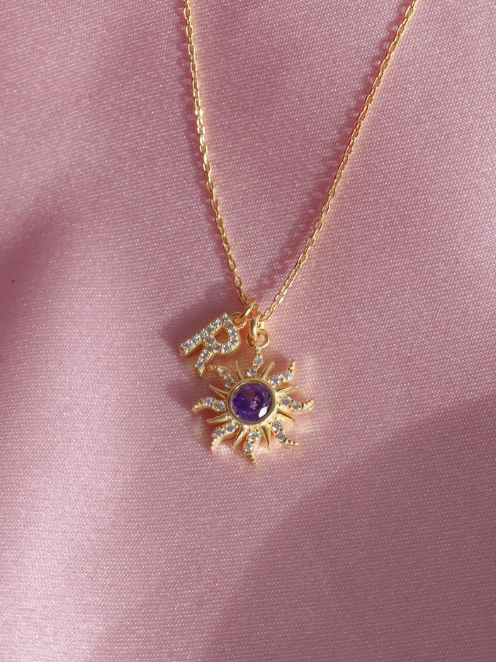 Rapunzel Sun Letter Necklace, 925 Sterling Silver, Princess Jewelry. A gold-colored necklace featuring a purple sun charm with lettering on it, displayed on a pink background.