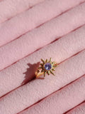 Rapunzel Sun Ring with a purple gemstone on a pink fabric background
