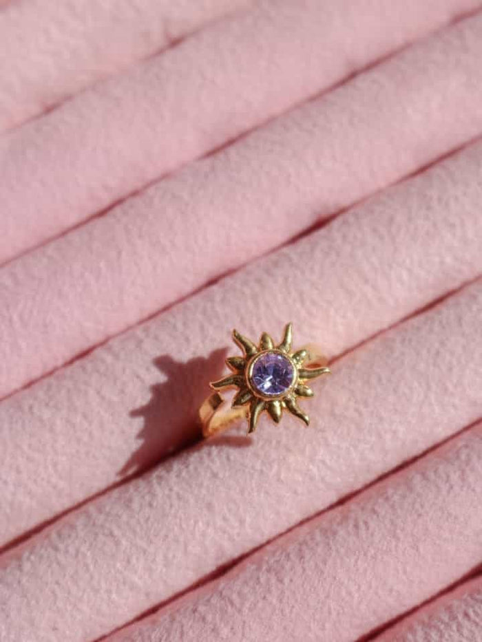 Rapunzel Sun Ring with a purple gemstone on a pink fabric background