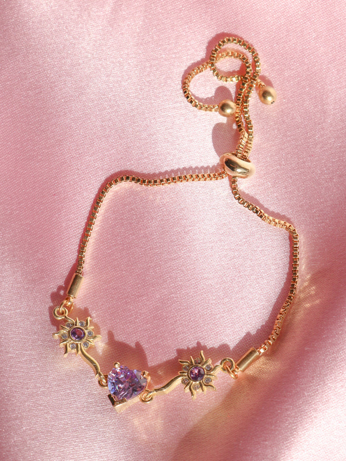 Rapunzel Sun With Heart Bracelet featuring a sun and heart charm with purple zirconia stones, displayed on a pink background.